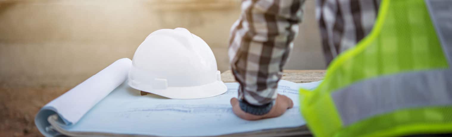 Rückansicht eines Arbeiters auf einer Baustelle welcher sich einen Bauplan ansieht