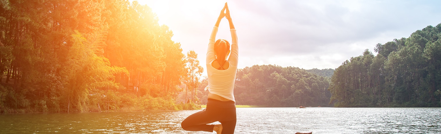 Eine Frau, die eine Yogafigur ausübt an einem Fluss in einer tropischen Umgebung